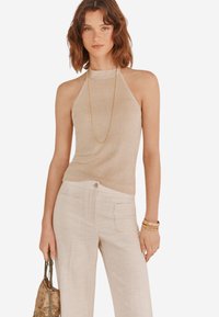 Beige Halftertop aus einem weichen, glänzenden Material, kombiniert mit hellen, strukturierten Hosen mit vorderen Taschen und einem Knopfverschluss.