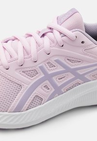 Primer plano de una zapatilla deportiva en tonos rosa y lavanda, con tejido de malla, cordones, superposiciones sintéticas y una suela blanca texturizada.