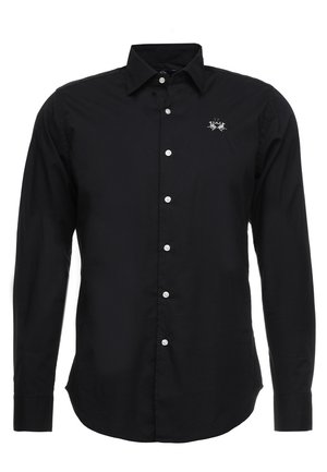 Chemise noire à manches longues avec boutons blancs et petit logo blanc brodé sur le côté gauche de la poitrine.