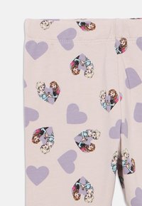 Lichtpaarse legging met een herhaald patroon van cartoonfiguren in hartjes, op een zachte beige achtergrond.