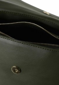 Interno di borsa in pelle verde con cerniera dorata. L'apertura presenta una chiusura a bottone scatto. Superficie testurizzata visibile.