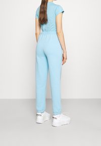 Ljusblå matchande set bestående av en figurnära kortärmad topp och avslappnade byxor; slätt tyg, elastisk midja och ribbade muddar.