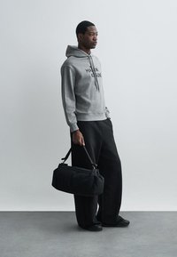 Grau Kapuzenpullover mit einem Frontlogo, kombiniert mit lockeren schwarzen Hosen und einer schwarzen Sporttasche. Sanfte Stofftexturen, lässiges Design.