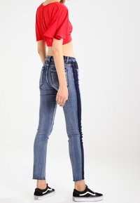 Červený krátký top s volnými rukávy, spárovaný s úzkými modrými džíny s tmavým bočním pruhům a třepeným lemem. Černé plátěné tenisky.