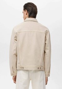 Beige denim jack met een gestructureerd ontwerp, voorzien van een klassieke kraag, rechte naden en metalen hardware bij de taille.