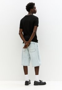 Un tricou negru cu mânecă scurtă, pantaloni șort din denim albastru deschis până la genunchi, șosete albe și pantofi negri; stând cu mâinile la spate.