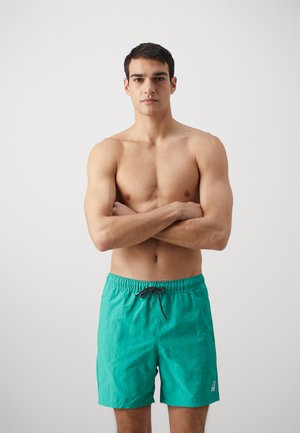 Pantaloni da bagno turchesi realizzati in tessuto leggero, con vita elastica e coulisse, e un piccolo logo sulla gamba inferiore.