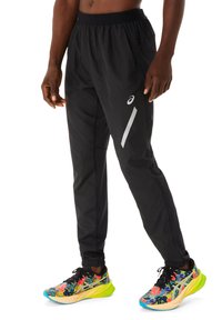 Jogging noir en matière athlétique avec une coupe ample, une taille élastique, des poches latérales et des accents réfléchissants. Associé à des chaussures de course multicolores.