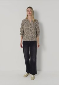 Blouse à imprimé animal en beige et noir, avec un col en V et des manches froncées. Associée à un jean noir à taille haute et des baskets légères.