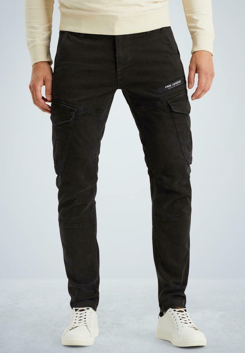 Schwarze Baumwollmischung Cargo-Hosen mit mehreren Taschen, slim-fit Design, verstärkten Nähten und einer strukturierten Oberfläche. Kombiniert mit weißen Sneakers.