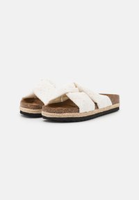 Sandales à glisser blanches en tissu tissé avec des brides croisées et des détails en œillets, semelle en liège, semelle intermédiaire en jute et semelle extérieure en caoutchouc noir.