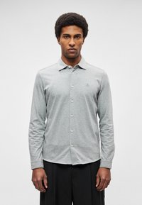 Camisa de botões de manga comprida em algodão cinza claro, com gola, logótipo subtilmente gravado no lado esquerdo do peito e fecho padrão com botões.