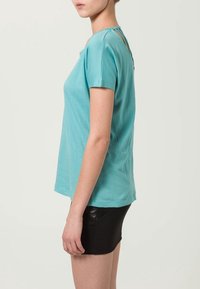 T-shirt turchese a maniche corte con una vestibilità rilassata, caratterizzato da un design con taglio unico sulla schiena, abbinato a una mini gonna nera.