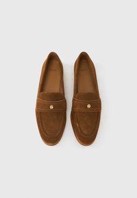 Brown suede loafers with a flat design, featuring a wide strap and gold logo accent. Smooth texture, rounded toe, and slip-on style.