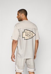 Ανοιχτό γκρι δίκτυο φανέλας με κατακόρυφες ρίγες, που διαθέτει ένα μεγάλο λογότυπο KC στο πίσω μέρος. Συνοδεύεται από κοντά σορτς, επίσης σε ανοιχτό γκρι τόνο.