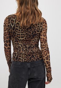 Leopard print long-sleeve top with a fitted design, sheer texture, and ruched detailing at the back, paired with black high-waisted jeans.