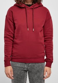 Sudadera con capucha en color granate con bolsillo frontal tipo canguro, capucha con cordón, puños y dobladillo acanalados, confeccionada en un tejido suave y texturizado.