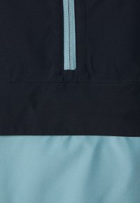 Fermeture éclair bleu clair sur un tissu à blocs de couleur bleu marine et bleu clair, montrant un gros plan des détails du vêtement et des coutures.