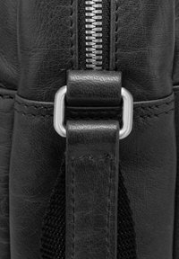Black leather bag detail featuring a silver zipper, a textured strap with an aluminum clasp, and stitched accents for durability.