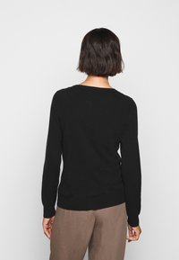Maglione nero con maniche lunghe, polsini e orlo a costine. Tessuto morbido, scollatura rotonda, design aderente, indossato con pantaloni marrone chiaro.