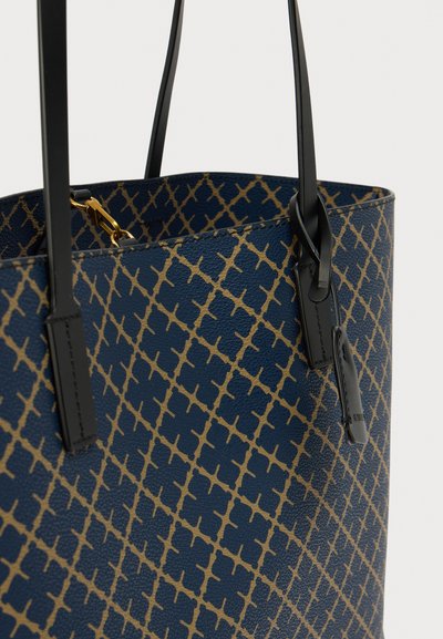 Sac cabas bleu marine avec une finition texturée, présentant un motif géométrique doré. Poignées en cuir noir et accents de mobilier doré.