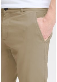 Beige Hosen mit glatter Textur, ausgestattet mit Seitentaschen, einem Knopfverschluss und einem taillierten Schnitt.