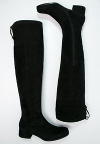 Botas de gamuza negra hasta la rodilla con tacón cuadrado, que cuentan con un zipper lateral y una textura suave. Incluyen una lengüeta para facilitar el uso.