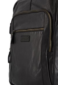 Czarny skórzany plecak z przednią kieszenią na zamek, teksturowaną powierzchnią, złotymi akcentami i oznaczeniem marki.