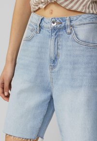 Shorts en denim bleu clair avec une taille haute, un ourlet effiloché et des effets d'usure subtils. Comprend un bouton à l'avant et des passants pour ceinture.