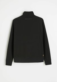 Czarny długi sweter z rękawami, z wysokim kołnierzem, widocznym przeszyciem na dole i mankietach oraz małą naszywką z logo na dolnej prawej stronie pleców.