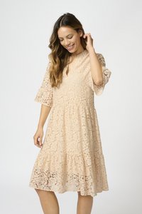 Spetsklänning i mjuk persikofärg med V-urringning, utsvängda ärmar, texturerade blommönster och en lager-på-lager fåll. Lätt och feminin design.