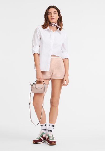 Weißes Hemd mit Knöpfen, rosa gerippte Shorts, rosa Handtasche, mehrfarbige Turnschuhe, gestreifte Socken, mit einem bedruckten Schal um den Hals.