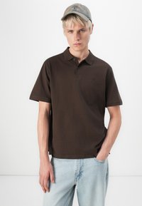 Bruine polo met korte mouwen, twee knopen bij de kraag, gecombineerd met lichtblauwe denim jeans. Licht gestructureerde stof, relaxte pasvorm.