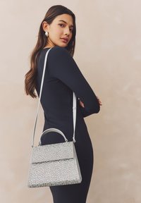 Zilveren handtas bedekt met fonkelende kristallen, met een gestructureerde vorm, handvat bovenaan en afneembare schouderriem; gladde textuur.