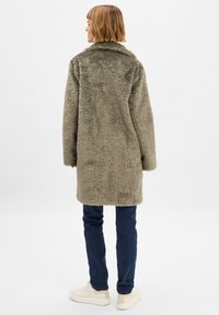 Olijfgroene faux fur jas met een kraag, lange mouwen, halflange lengte, gestructureerd oppervlak, gecombineerd met donkerblauwe jeans en witte sneakers.