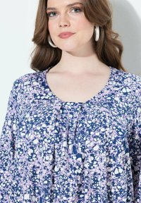Bluse mit floralem Muster, tiefem Rundhalsausschnitt, fließendem Design und einer Mischung aus Marineblau, Lila und Weiß in einem leichten Stoff.