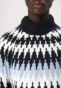 Maglione a collo alto lavorato a maglia, con un motivo a zigzag in blu navy, nero, bianco e azzurro chiaro. Finitura in tessuto testurizzato.