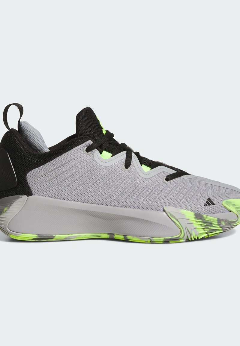 Chaussure de sport grise avec accents noirs, tige en maille texturée, détails en vert néon et semelle à motifs. Présente une languette au niveau du talon.