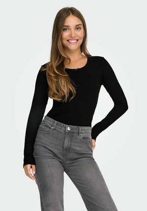 Top nero a costine con maniche lunghe e scollatura rotonda abbinato a jeans grigi a vita alta. Texture liscia, design aderente, dettagli discreti di bottoni e tasche.