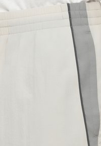 Jasnoszare szorty z elastycznym pasem, z kontrastowym ciemnoszarym paskiem po bokach oraz gładką, teksturowaną tkaniną.