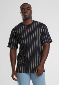 Tricou negru cu dungi verticale albe, mâneci scurte, decolteu rotund, având un logo brodat roșu în zona stângă a pieptului.