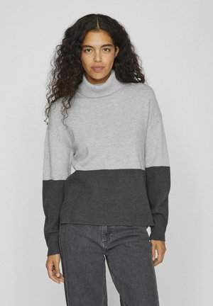 Suéter de cuello alto gris y gris oscuro con textura acanalada, presenta hombros caídos y un corte relajado, combinado con jeans oscuros.