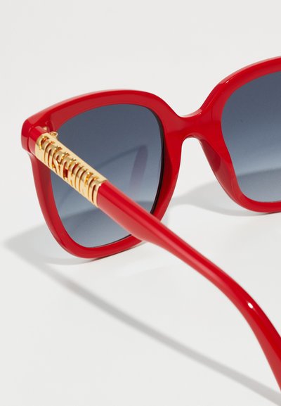 Ochelari de soare roșii supradimensionați cu lentile întunecate și degrade. Se remarcă prin detalii aurii pe brațe, un cadru din plastic elegant și o finisare lucioasă.