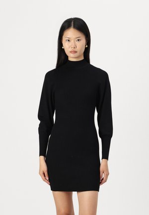Schwarzes, geripptes Kleid mit hohem Hals und langen, enganliegenden Ärmeln. Die Textur ist weich, mit einer figurbetonten Silhouette, die die Kurven betont.