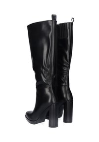 Botas de charol negras hasta la rodilla, con un tacón ancho alto, punta redonda y cierre de cremallera en la parte posterior para facilitar el uso.