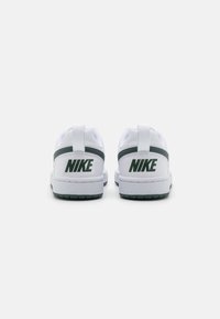 Bele superge Nike v beli barvi z zelenimi akcenti, ki vključujejo teksturiran zadnji del, zanka za obuvanje in izstopajoč logo na peti. Ravna podplat s črtasto strukturo.