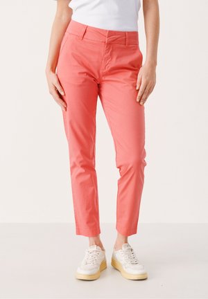 Pantalon slim rose clair avec une texture lisse, poches avant et taille plate. Associé à des baskets blanches et un top ajusté.