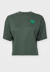 Kortsleev, cropped t-skjorte laget av mykt grønt stoff, med rund hals og et brodert sirkulært merke på brystet.