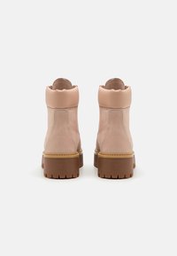 Botines de ante rosa con puntera redondeada, cuello acolchado y suela de goma marrón con profundos relieves para mayor tracción. Acabado suave, diseño minimalista.