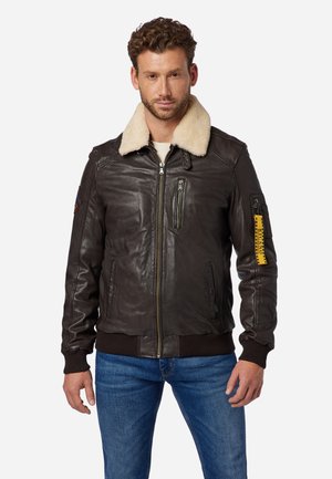 Giacca bomber in pelle marrone con collo in shearling, tasche con cerniera, polsini e orlo a costine, e un accento giallo sulla manica sinistra.